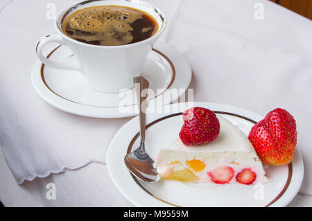 Ein Stück Erdbeer Dessert auf eine weiße Platte mit einer Tasse Kaffee Stockfoto