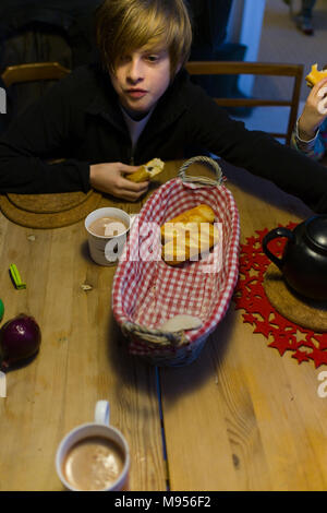 Eine noch junge mit den rotblonden Haaren sitzt um einen hölzernen Tisch zu Hause in Frankreich, essen Pain au Chocolate von einem Korb. Stockfoto