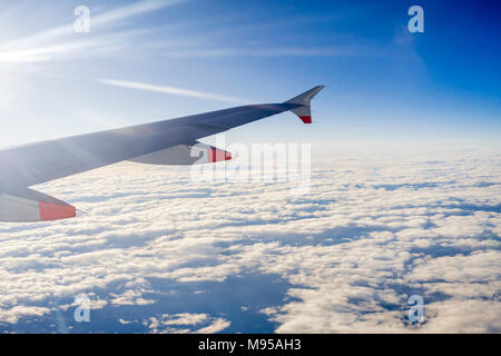 Blick aus dem Flugzeug Fenster im Flug auf die Flugzeugflügel mit blauem Himmel und Stratocumulus Wolken sichtbar Stockfoto