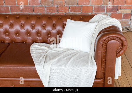 Braun Sofa, auf dem liegen eine weisse Decke und Kissen Stockfoto