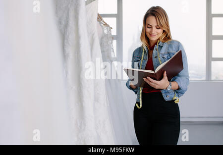 Frau Schneider schreiben in einem Tagebuch im Stehen Hochzeit Kleid zu speichern. Weibliche kleid designer Arbeiten in bridal Clothing Store. Stockfoto