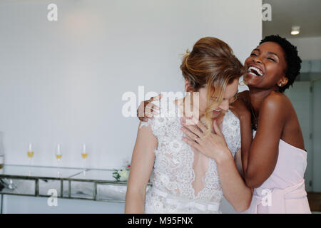 Fröhliche junge Braut und Brautjungfern am Tag der Hochzeit im hotel zimmer Spaß haben. Gerne wunderschöne Braut im weißen Kleid Spaß mit Brautjungfer. Stockfoto