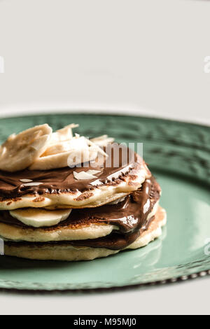 Amerikanische Pfannkuchen mit Schokolade und Banane auf ein Pastell grün rustikale Platte Stockfoto
