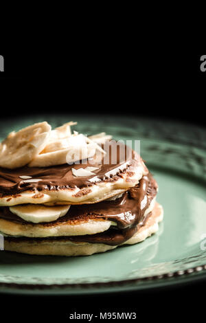 Amerikanische Pfannkuchen mit Schokolade und Banane auf ein Pastell grün rustikal mit schwarzen Hintergrund Platte Stockfoto