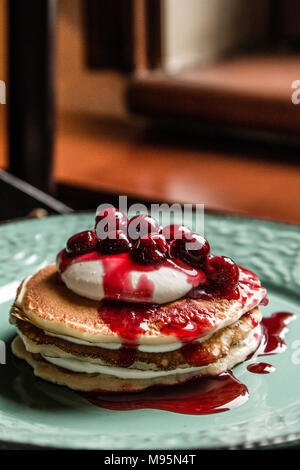 Amerikanische Pfannkuchen mit Früchten Creme und Kirschen auf einem Pastellgrün rustikale Platte und tägliche Licht Stockfoto