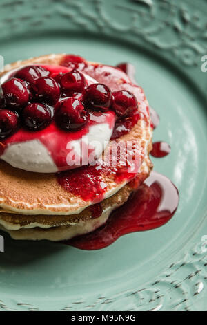 Amerikanische Pfannkuchen mit Früchten Creme und Kirschen auf einem Pastellgrün rustikale Platte von oben Stockfoto