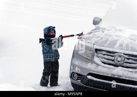 Ein Junge (5 Jahre alt) Bürsten frisch gefallenen Schnee von einem Auto in Quebec, Kanada Stockfoto