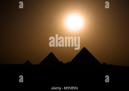 Eine volle Sonne ist nur wenige Minuten von der Einstellung hinter der Gizeh Pyramiden komplexe verlassen die alten Strukturen in der Silhouette, Kairo, Ägypten Stockfoto