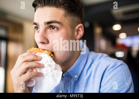 Gerne schöner Mann Burger essen im Restaurant Stockfoto