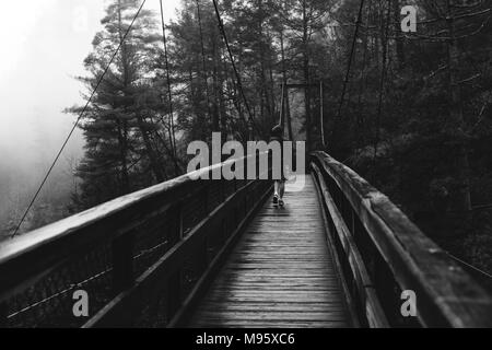 Ein Teenager kreuzt die Suspension Bridge an einem nebligen und verregneten Morgen an Tallulah Gorge State Park in Georgia, USA. Stockfoto