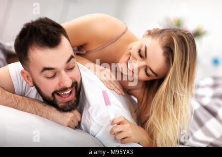 Glückliches Paar mit Schwangerschaft Test im Schlafzimmer Stockfoto