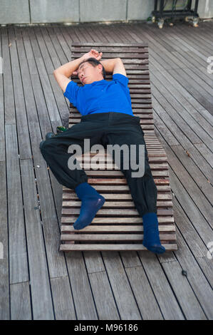 22.03.2018, Singapur, Republik Singapur, Asien - ein Mann hält ein Nickerchen auf einem hölzernen Liegestuhl an der Marina Bay. Stockfoto