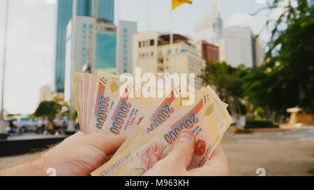 Mann erzählt Vietnamesisch Geld. Zweihundert und ein Hunderttausendstel der Banknote auf dem Hintergrund der Innenstadt von Ho Chi Minh Stadt. Stockfoto