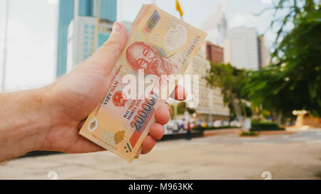 Mann erzählt Vietnamesisch Geld. Zweihundert und ein Hunderttausendstel der Banknote auf dem Hintergrund der Innenstadt von Ho Chi Minh Stadt. Stockfoto