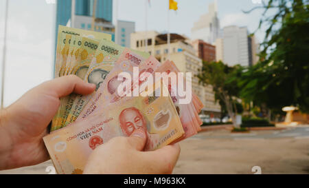 Mann erzählt Vietnamesisch Geld. Zweihundert und ein Hunderttausendstel der Banknote auf dem Hintergrund der Innenstadt von Ho Chi Minh Stadt. Stockfoto