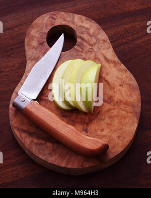 Schneiden Sie in Scheiben geschnitten und Apple mit klappbarer Obst Messer auf einem olivenholz Brett. Stockfoto