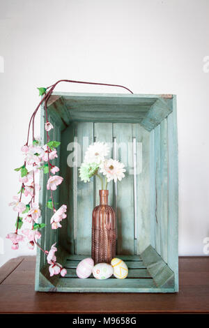 Ostereier und Frühlingsblumen, gerbera oder Daisy, in einem Vintage rosa Vase innerhalb eines alten Holz- Obst Kiste Stockfoto