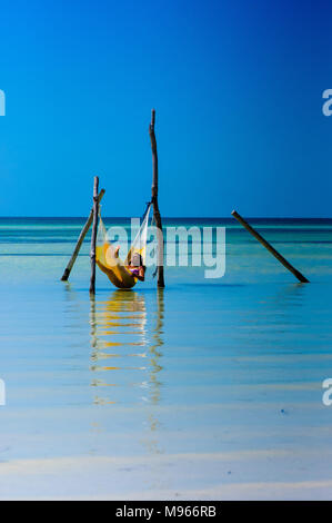 Frau Entspannung in einem Hängematte über ein kristallklares Wasser in der Karibik mit blauem Himmel in Holbox, Mexiko Stockfoto
