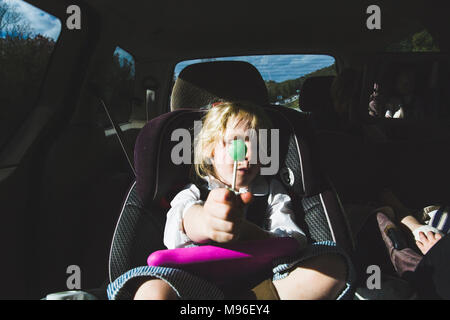 Mädchen mit grünem Lollipop in Autositz sitzen Stockfoto