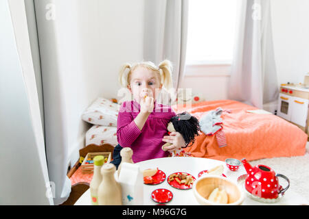 Mädchen mit Puppe sitzend am Tisch essen Stockfoto