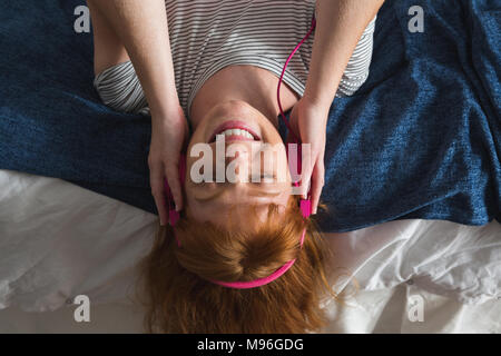 Frau mit Kopfhörer Musik hören im Schlafzimmer Stockfoto
