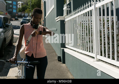 Frau Kontrolle der Zeit auf Ihrem smartwatch beim Gehen auf einem Bürgersteig Stockfoto