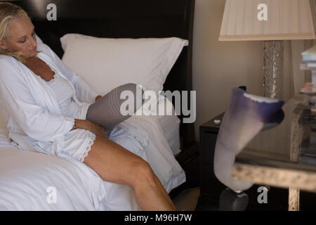 Frau mit Prothese Socken tragen im Schlafzimmer Stockfoto