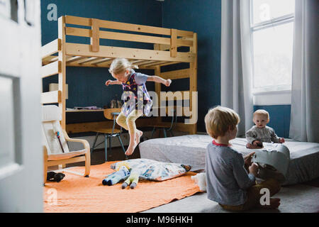 Mädchen springen im Schlafzimmer neben zwei weitere Kinder. Stockfoto