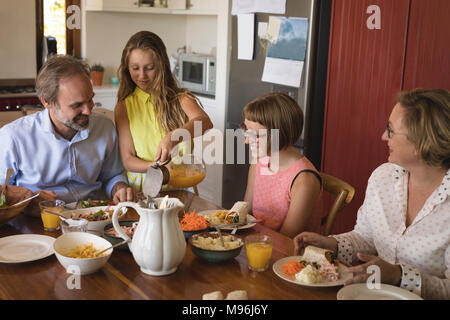 Tochter mit Saft zu ihrer Familie in der Küche Stockfoto