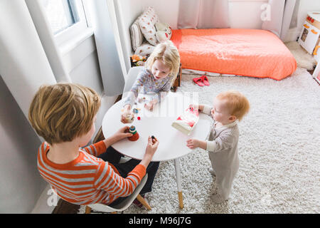 Zwei Kinder und Baby spielt um einen weißen Tisch Stockfoto