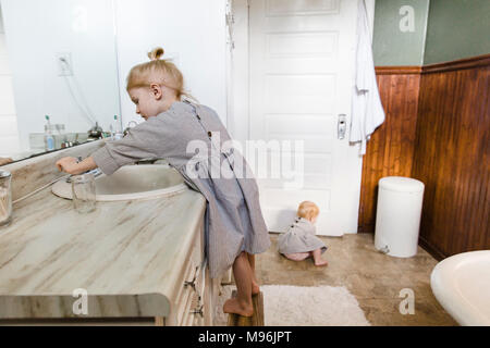 Mädchen mit Waschbecken, während Baby sitzt auf Boden im Badezimmer Stockfoto