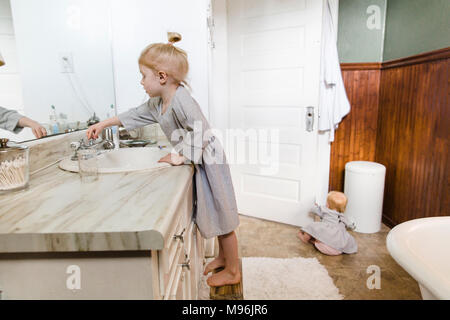 Mädchen mit Waschbecken, während Baby sitzt auf Boden im Badezimmer Stockfoto