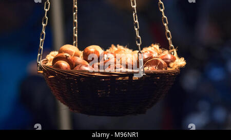 Kleine hölzerne Korb voller gerösteten Kastanien in der Nacht Weihnachten Street Market, Korb mit Kastanien hängen unter hellen Licht. Stockfoto