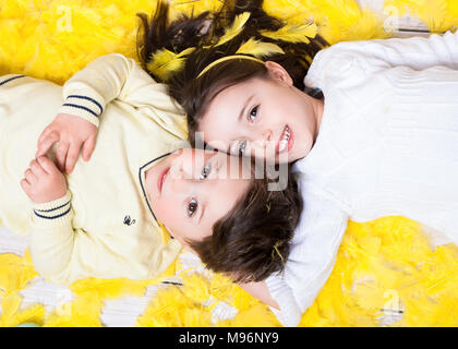 Mädchen und Jungen (4-6) liegen auf Gelbe Feder lächelnd. Frühling und Ostern Konzept Stockfoto