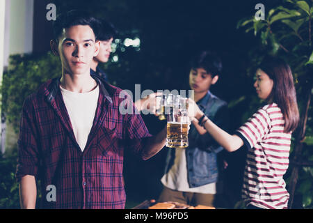 Asiatische Gruppe von Freunden in Außenbereich Garten Grill Lachen mit alkoholfreien Bier Getränke bei Nacht Stockfoto