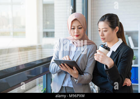 Muslimische Geschäftsfrau, die die traditionellen Schal trägt, sagt die Mitarbeiter nach ihrer Meinung. Sie beide tragen Anzug im Büro. Eine u Stockfoto