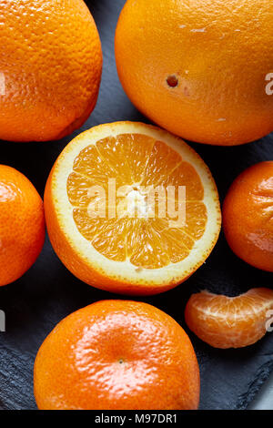 Hohen Winkel noch leben Blick auf geschnittene Ruby orange und Tangerine arrangiert zusammen auf der rechten Seite des schwarzen Stein Schneidbrett über weiße strukturierte Ba Stockfoto