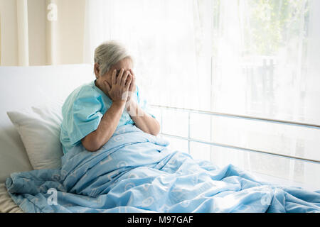 Asiatische gedrückt ältere Frau Patienten liegend auf Bett Blick aus dem Fenster im Krankenhaus. Ältere Frau Patienten ist froh, von der Krankheit erholt. Stockfoto