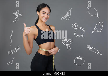 Lächelnde Frau messen ihre Taille Linie und setzen Ihre Daumen hoch Stockfoto