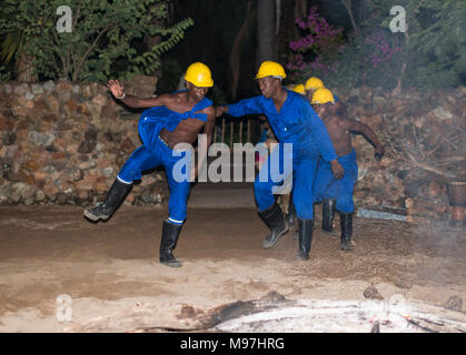 Hoedspruit, Südafrika, 09-03-2014, afrikanischer Mann tanzen in traditioneller Kleidung mit Helm und blaumann als Sklaven bergleute am Lagerfeuer für die touri Stockfoto