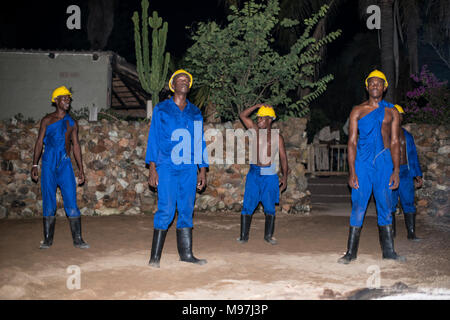 Hoedspruit, Südafrika, 09-03-2014, afrikanischer Mann tanzen in traditioneller Kleidung mit Helm und blaumann als Sklaven bergleute am Lagerfeuer für die touri Stockfoto