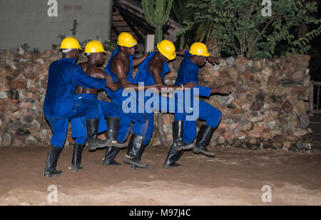 Hoedspruit, Südafrika, 09-03-2014, afrikanischer Mann tanzen in traditioneller Kleidung mit Helm und blaumann als Sklaven bergleute am Lagerfeuer für die touri Stockfoto