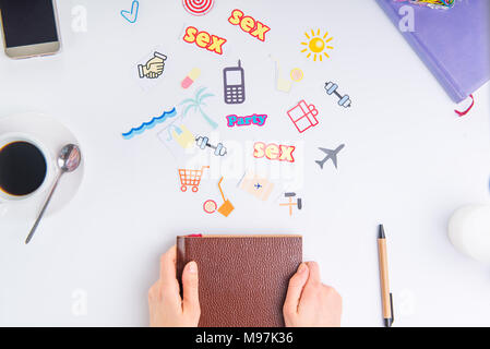 Ansicht von oben croped weibliche Hände halten Organizer und bunte Symbole Maßnahmen am Arbeitsplatz mit Schreibwaren und Kaffee geschlossen. Creative co Stockfoto