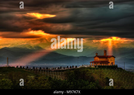Zwei klingen von Licht durch die Wolken und scheinen die Kapelle und der Obelisk des Partisanen Schrein, Bastia Mondovì, Piemont, Italien. Stockfoto