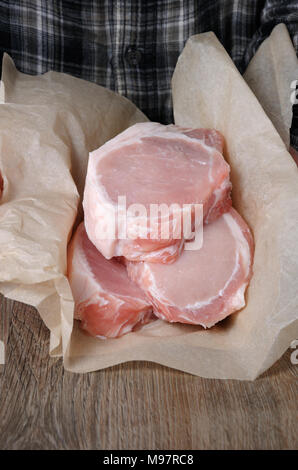 Ein Haufen von frischen gehackten rohes Schweinefleisch Steaks über die Knochen in Geschenkpapier in den Händen eines Mannes Stockfoto