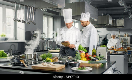 Zwei berühmte Köche sprechen über Ihre Video Blog während der Verwendung von Tablet Computer. Sie arbeiten auf einem großen Restaurant Edelstahl professionelle Küche. Stockfoto