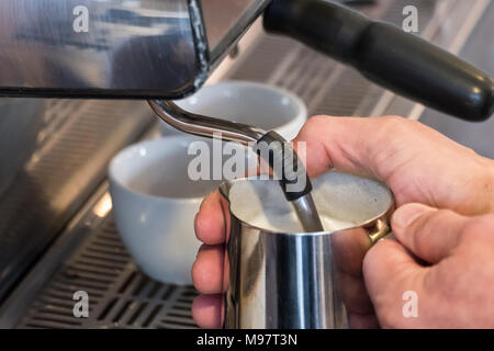 Barista dämpfen und Aufschäumen der Milch in Edelstahl Zuhaltung mit Espresso maching für Cappuccino oder Latte Stockfoto