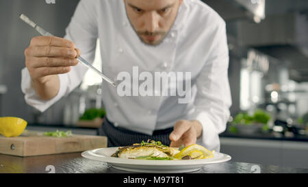 Berühmten Koch schmückt sein besonderes Fischgericht mit einigen Grüns. Er arbeitet in einer modernen Küche. Stockfoto