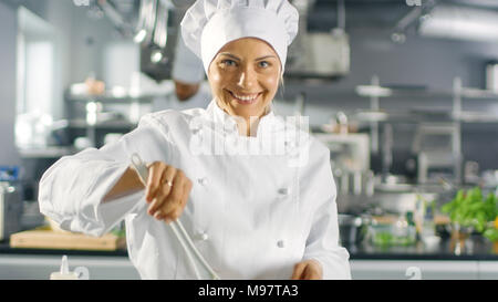In einem berühmten Restaurant weiblichen Koch bereitet Salat und lächelnd auf eine Kamera. Sie arbeitet in einem großen, modernen Küche. Stockfoto