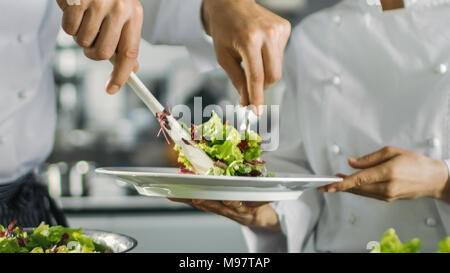 In einem berühmten Restaurant Koch bereitet Salat und legt es auf einen Teller. Arbeiten in einem großen, modernen Küche. Stockfoto